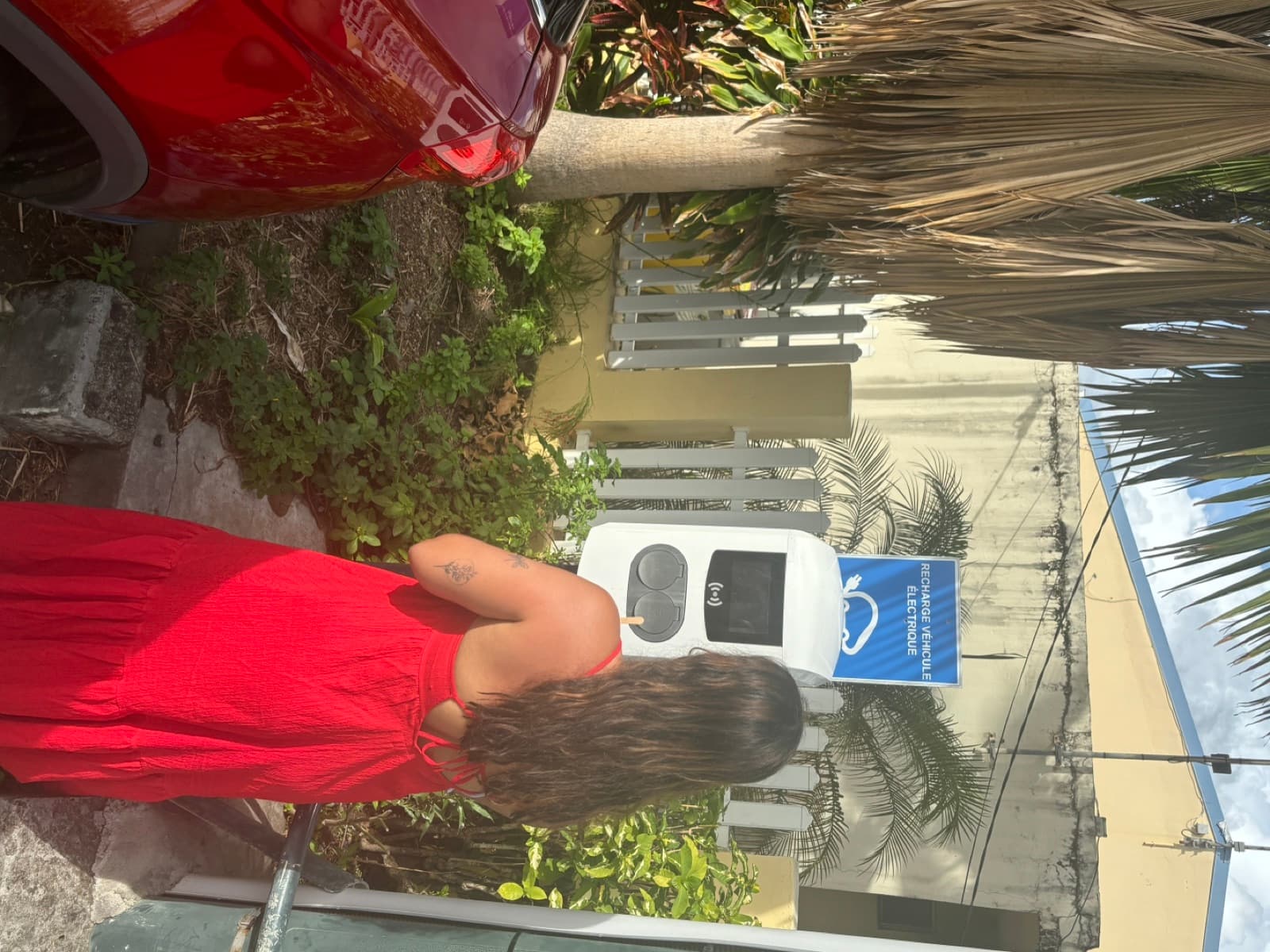 Cliente EZdrive en robe rouge devant une borne de recharge publique en Outre-mer